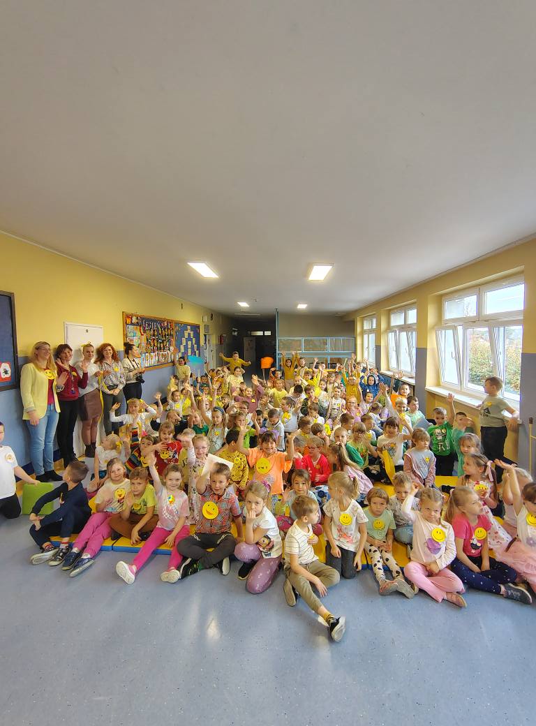 Zdjęcie grupowe uczniów z klas najmłodszych mających przypięte na bluzkach w żółte emotki z uśmiechami.