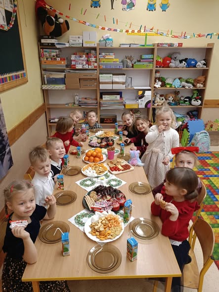 Uczniowie klasy 0a siedzą przy stolikach i częstują się słodkościami i mandarynkami.