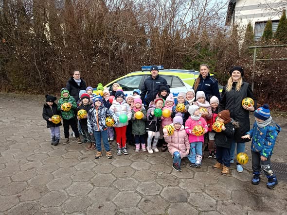 Uczniowie klas zero stoją przed radiowozem wraz z policjantami i opiekunami.