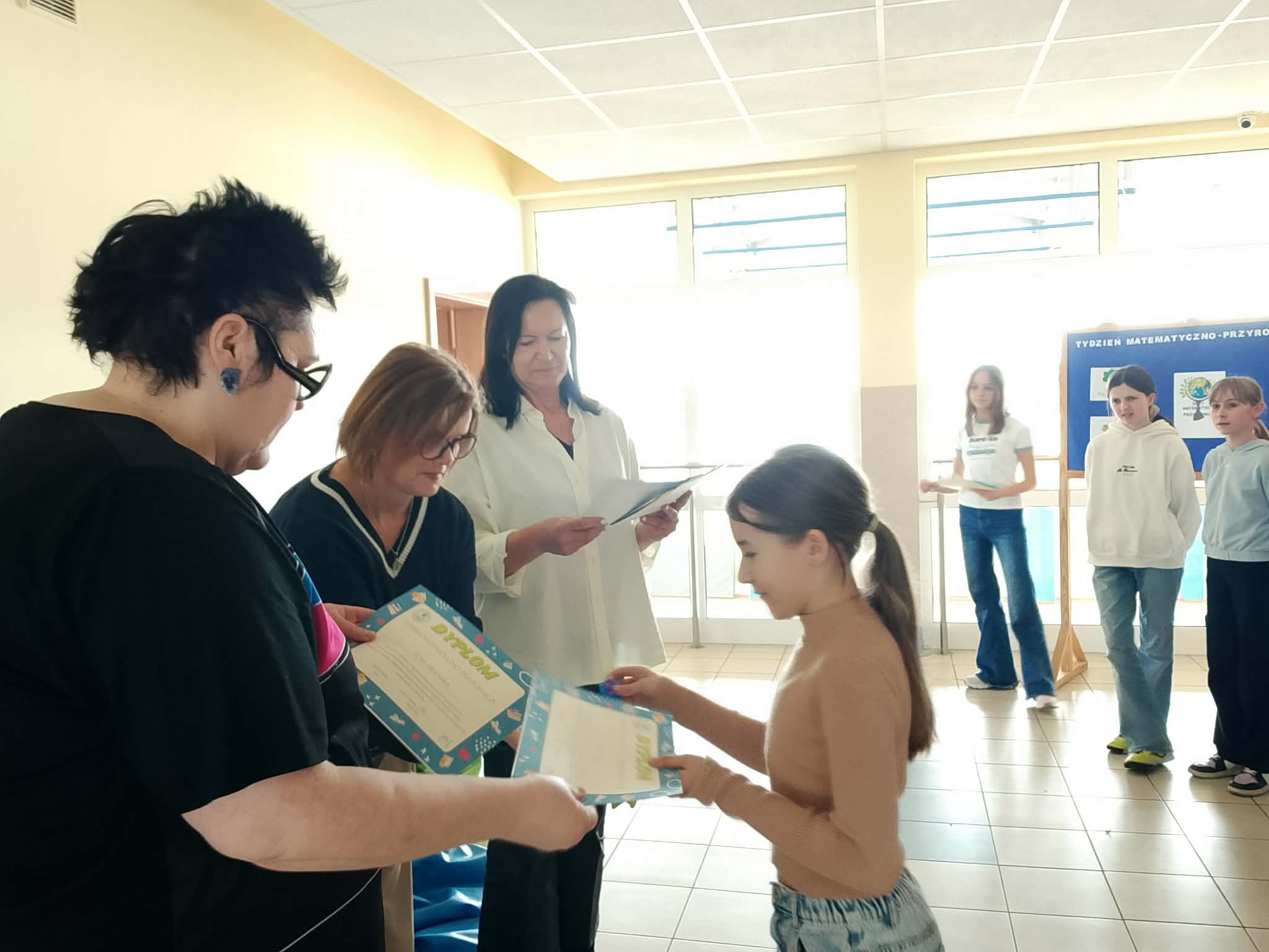 Uczennica odbiera dyplom i upominek od Pani Dyrektor. W tlen nauczycielka matematyki i biologii.
