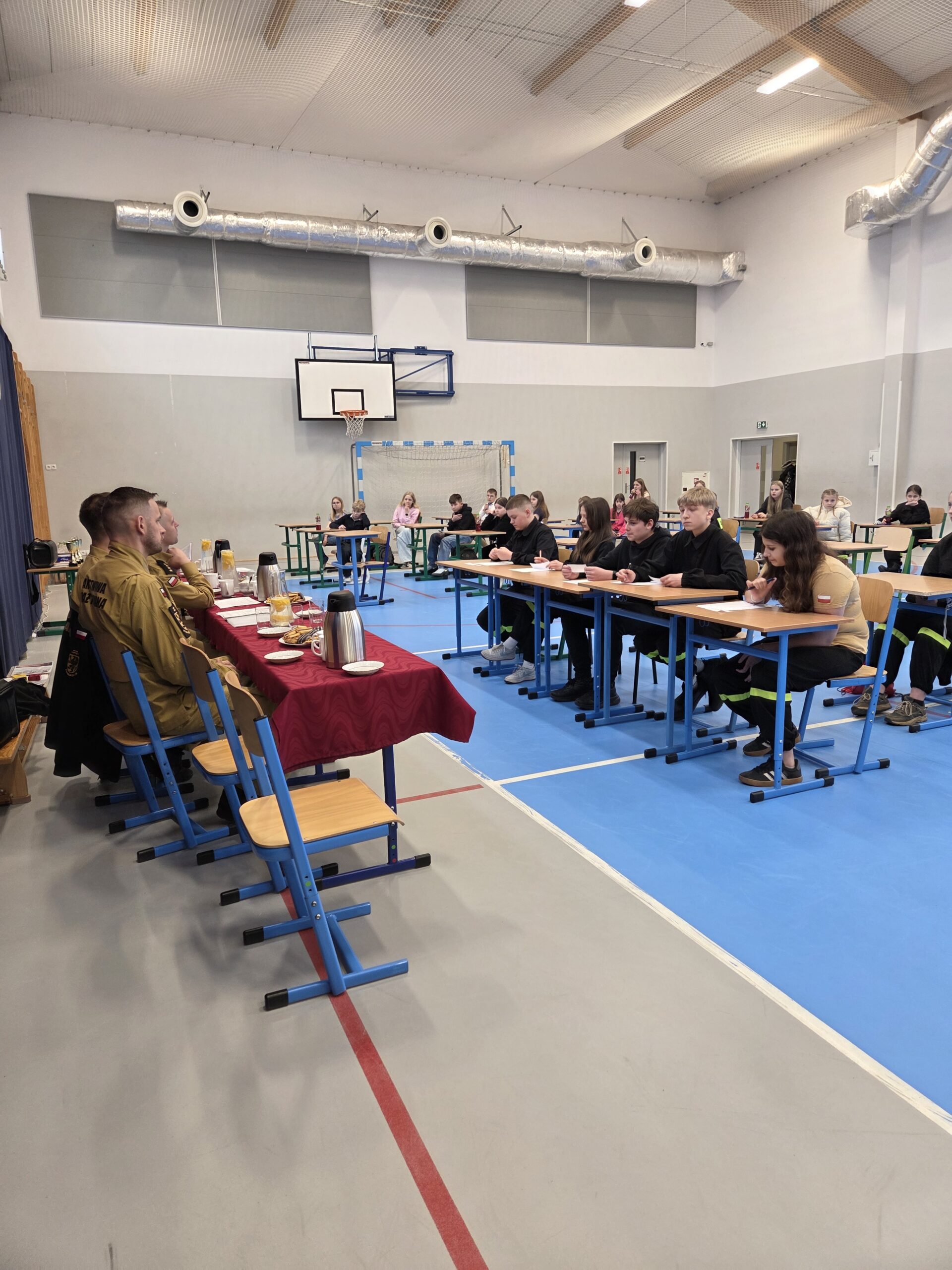 Uczniowie siedzą przed komisją i odpowiadają na pytania.