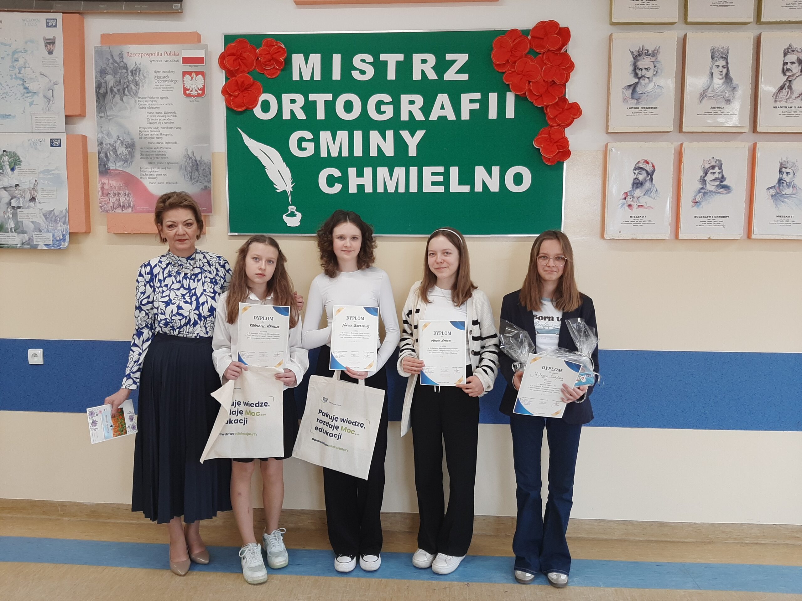 Uczennice wraz z opiekunem trzymają w ręku dyplomy i upominki w tle gazetka Mistrz Ortografii Gminy Chmielno.