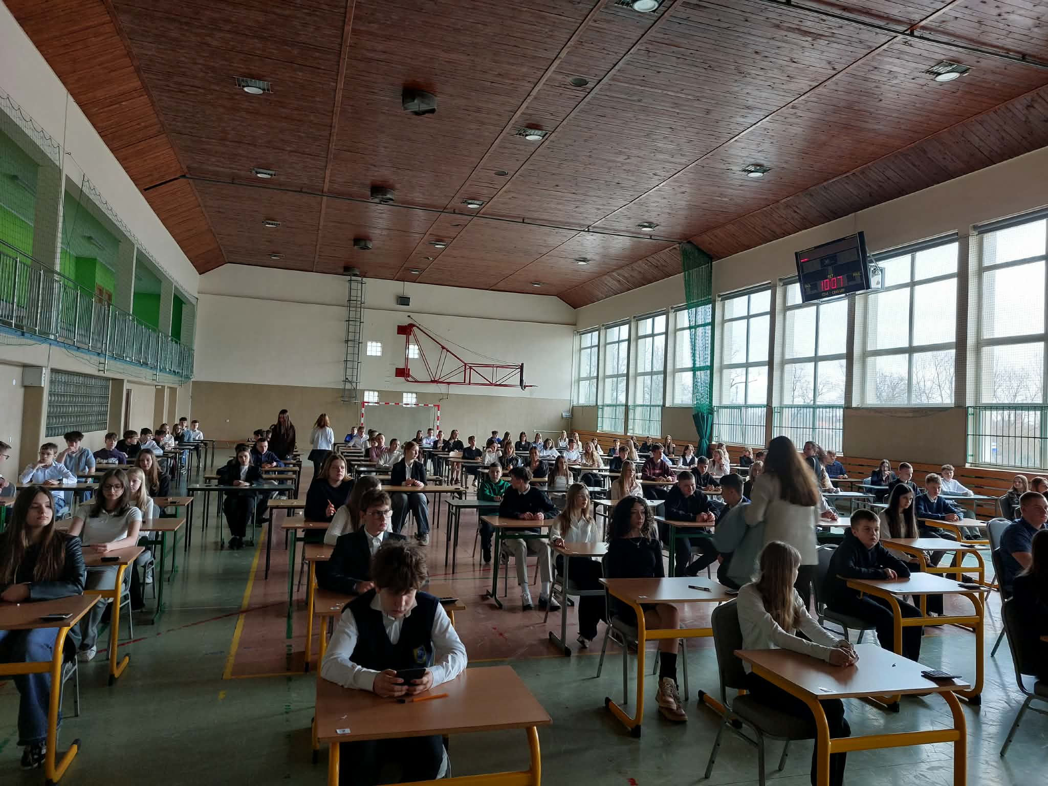 Uczniowie na hali sportowej podczas pisania testu.