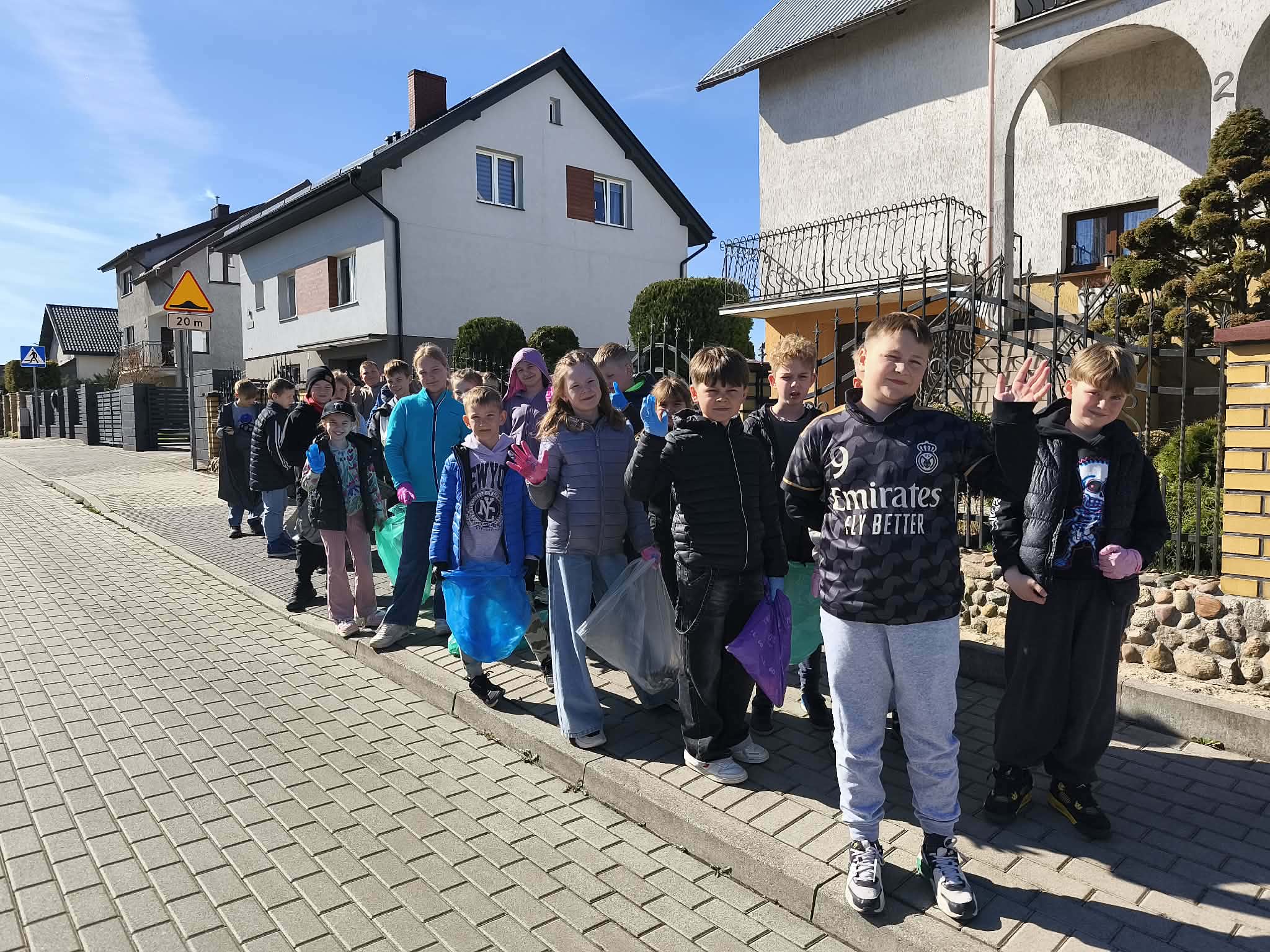 Uczniowie klasy 3 podczas akcji sprzątania świata przechodzą ulicami osiedla koło szkoły.