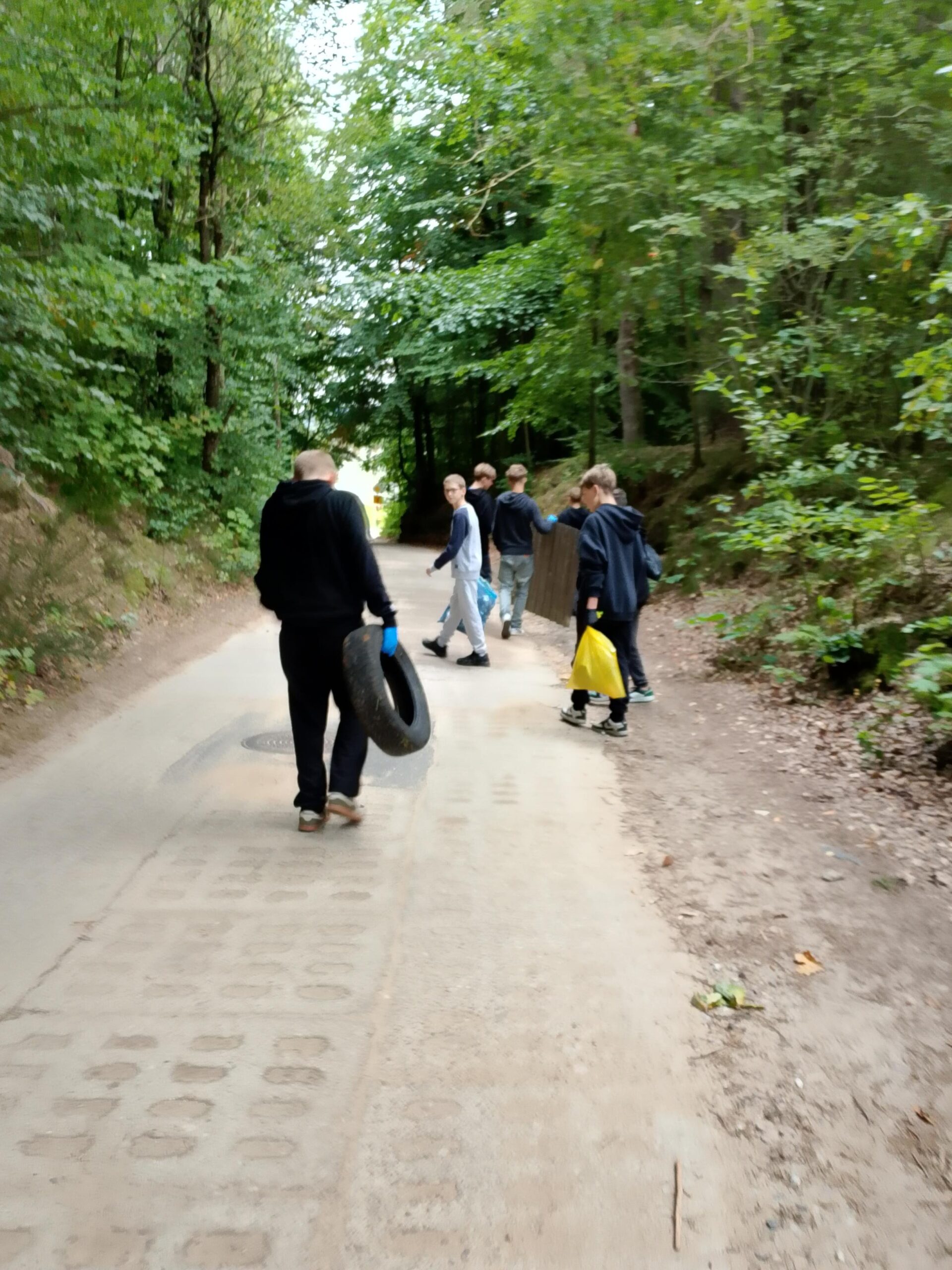 Uczniowie klasy 7b niosą śmieci, które znaleźli w lesie.
