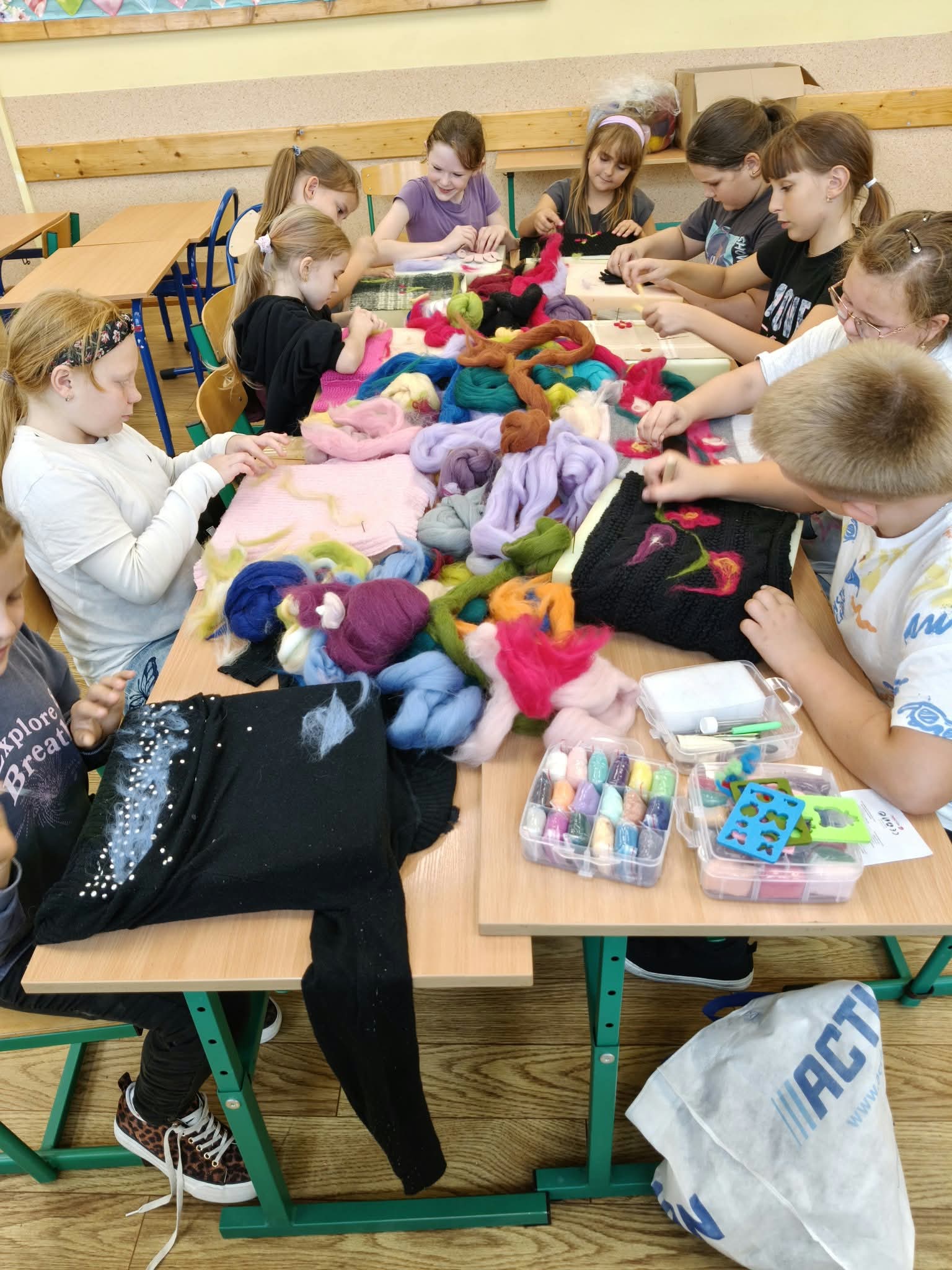 Grupa uczniów klas 4–5 siedzi przy stole i wykonuje prace techniką filcowania podczas zajęć Małej Pracowni Krawieckiej.