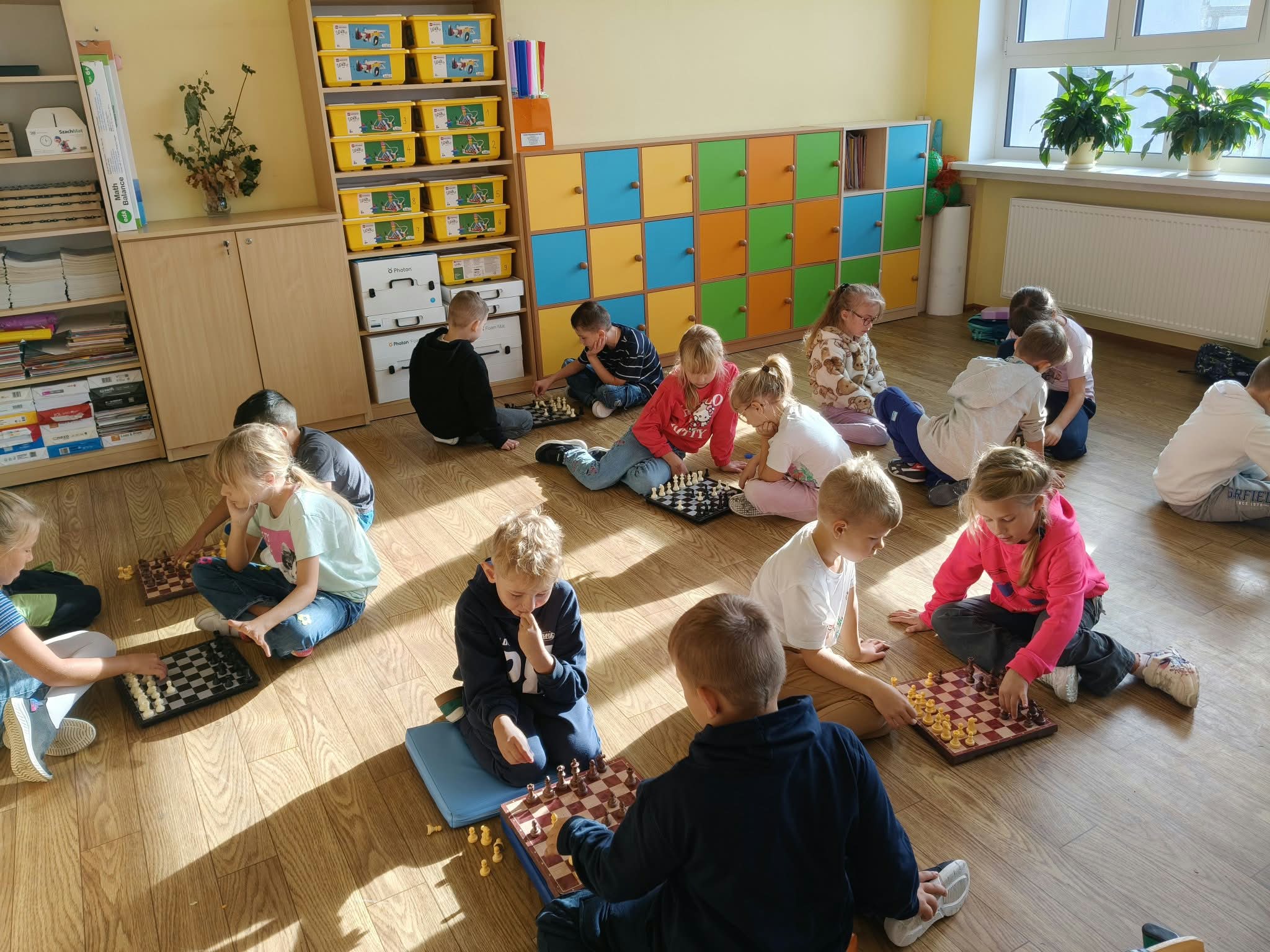 Uczniowie grają w szachy w parach na podłodze sali.