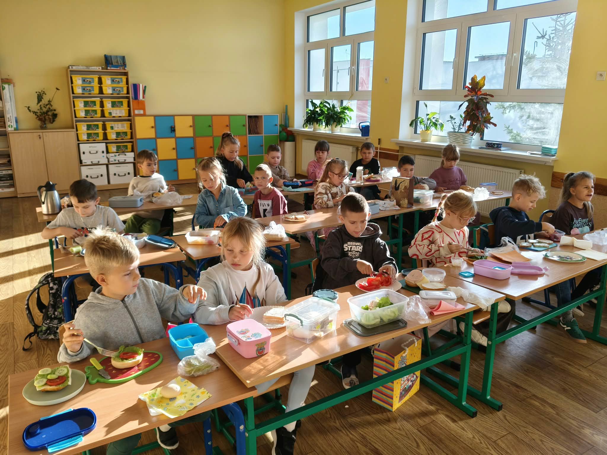 Uczniowie siedzą w ławkach i przygotowują zdrowe kanapki.